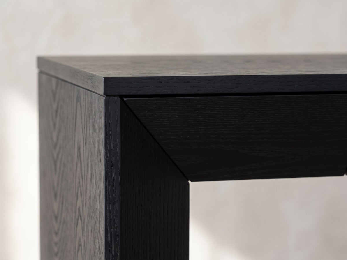 Close-up of the Cellamare Black Ash Veneer Waterfall Console Table: the mitred corner where the thin top and angled front band turn down into a slab leg