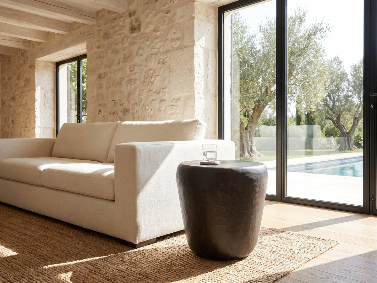 Cervara Rustic Bronze Metal Drum Side Table beside a linen sofa in a poolside villa