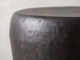 Close-up of the Cervara Rustic Bronze Metal Drum Side Table: the rolled rim and hammered shoulder of the bronze drum
