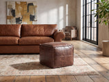 Cervo Distressed Brown Genuine Leather Square Pouf on a vintage rug in front of a leather sofa in an industrial loft