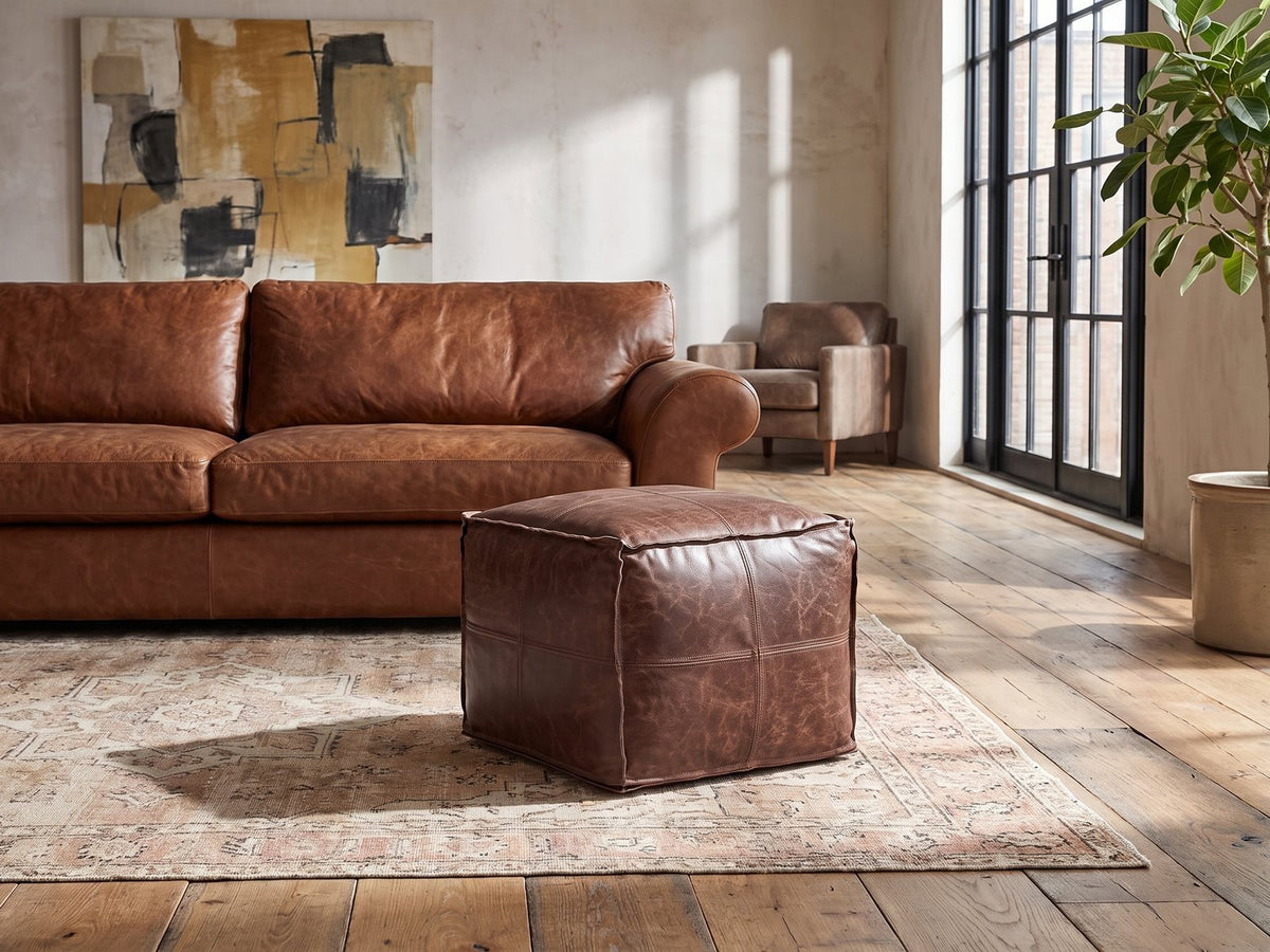 Cervo Distressed Brown Genuine Leather Square Pouf on a vintage rug in front of a leather sofa in an industrial loft