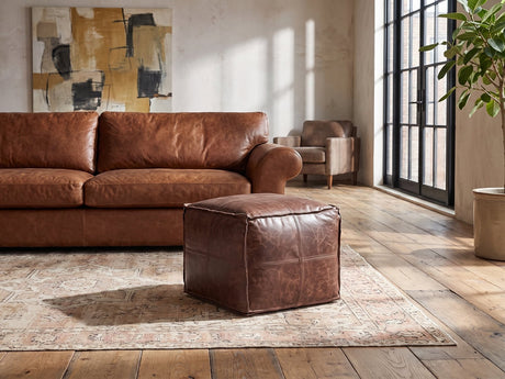 Cervo Distressed Brown Genuine Leather Square Pouf on a vintage rug in front of a leather sofa in an industrial loft