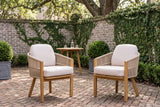 Two Chiaramonte dining armchairs on a herringbone brick courtyard in front of an old grey brick wall with creeping fig, a teak bistro table behind (table not included)