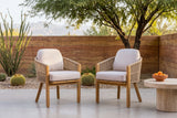 Two Chiaramonte dining armchairs on a polished concrete patio, a banded rammed-earth wall, a mesquite tree and barrel cacti behind (side table not included)
