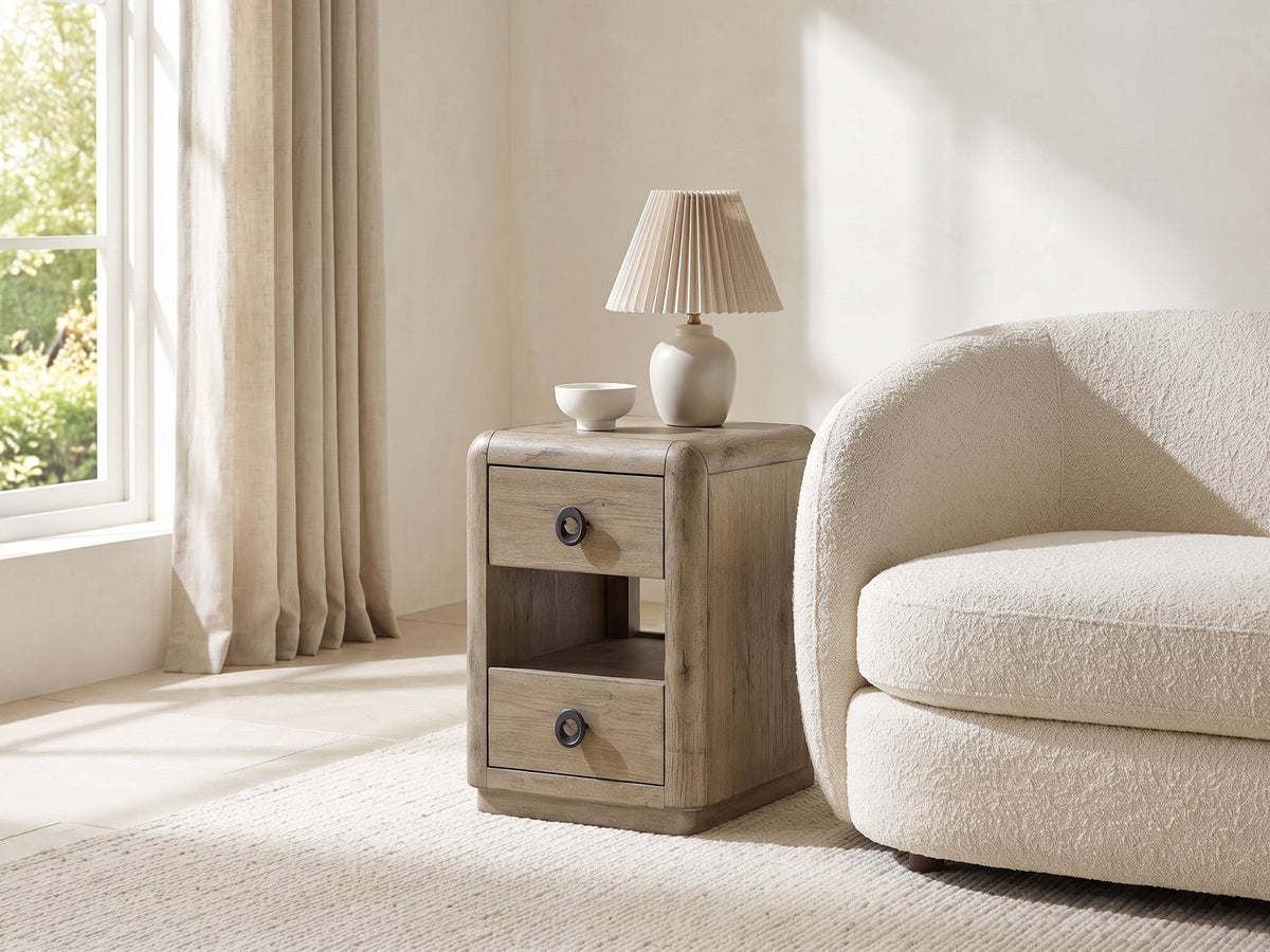 Chiaromonte Knotty Oak Veneer Two-Drawer Side Table with a lamp and a ceramic bowl beside a cream boucle armchair in a bright plaster room