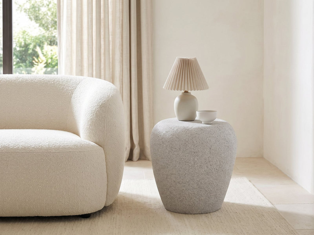 Cilento Speckled Grey Fiberglass Pebble Side Table with a lamp and a ceramic bowl beside a cream boucle sofa in a bright plaster room