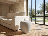 Cilento Speckled Grey Fiberglass Pebble Side Table beside a linen sofa in a poolside villa