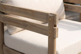 Close-up of a Cinisi arm: the two light brown acacia rails and the round front leg with brass-coloured screws, beside the beige cushions