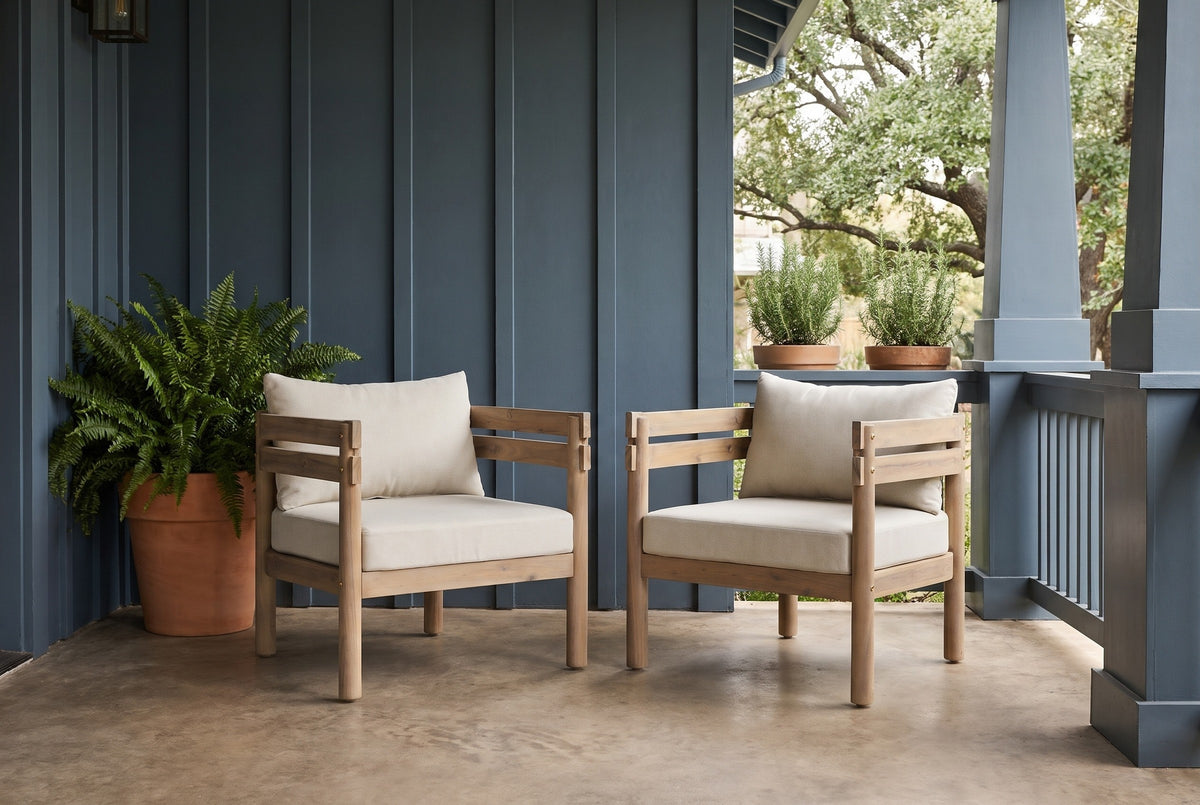 Two Cinisi acacia club chairs on warm grey stained concrete on an Austin porch, a slate-blue board-and-batten wall and a live oak behind (plants not included)