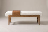 The Citerna bench seen from the long side on a light studio backdrop: ivory boucle cushion, honey-brown rail, four tapered legs and the wood tray
