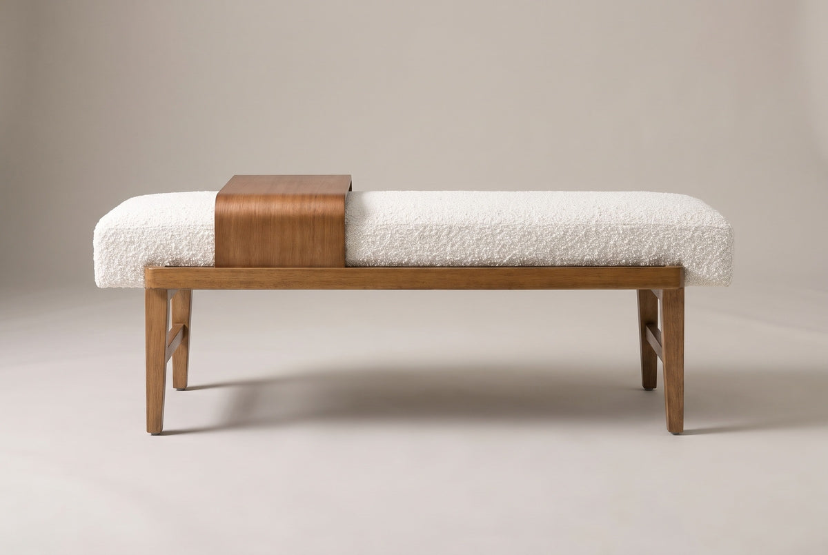 The Citerna bench seen from the long side on a light studio backdrop: ivory boucle cushion, honey-brown rail, four tapered legs and the wood tray