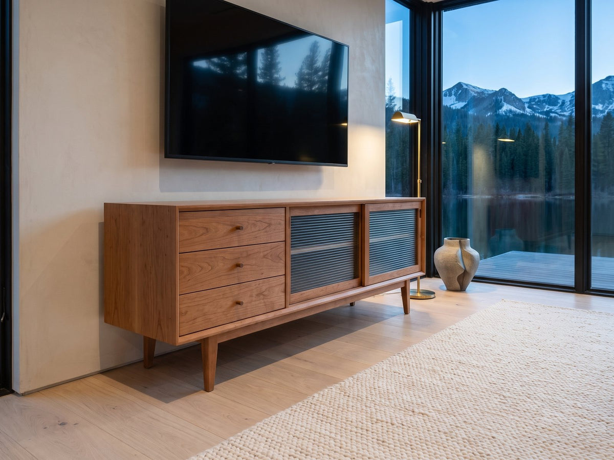 Cividale Solid Cherry Media Console seen from the side, under a wall-mounted screen in a mountain lake house at dusk