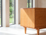 Close-up of the Cividale Solid Cherry Media Console: the dovetailed corner joint of the solid cherry case and the round tapered leg below it