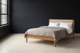 Civitella light walnut bed with a beige headboard against a charcoal wall in a Detroit loft, a tall black steel window at the left