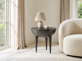 Colledara Cast Aluminum Bowl Side Table with a lamp and a ceramic bowl beside a cream boucle armchair in a bright plaster room