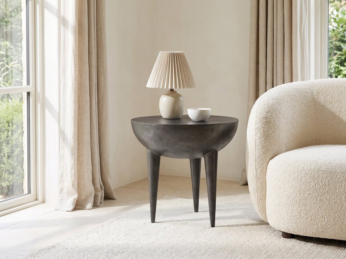 Colledara Cast Aluminum Bowl Side Table with a lamp and a ceramic bowl beside a cream boucle armchair in a bright plaster room