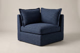 A single Comiso corner seat in navy slipcovers with two back pillows, on a light studio backdrop