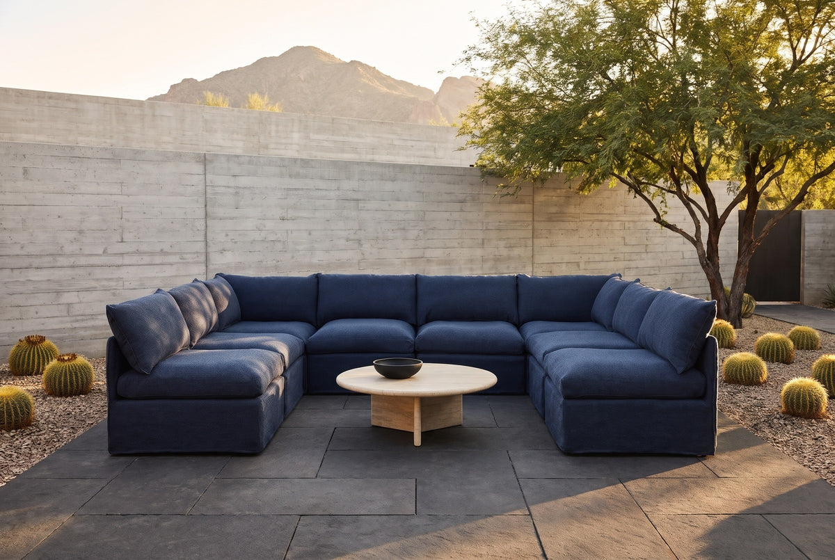 Comiso navy U-shaped outdoor sectional in a Paradise Valley, Arizona courtyard at golden hour, a board-formed concrete wall, basalt pavers and golden barrel cacti (coffee table not included)
