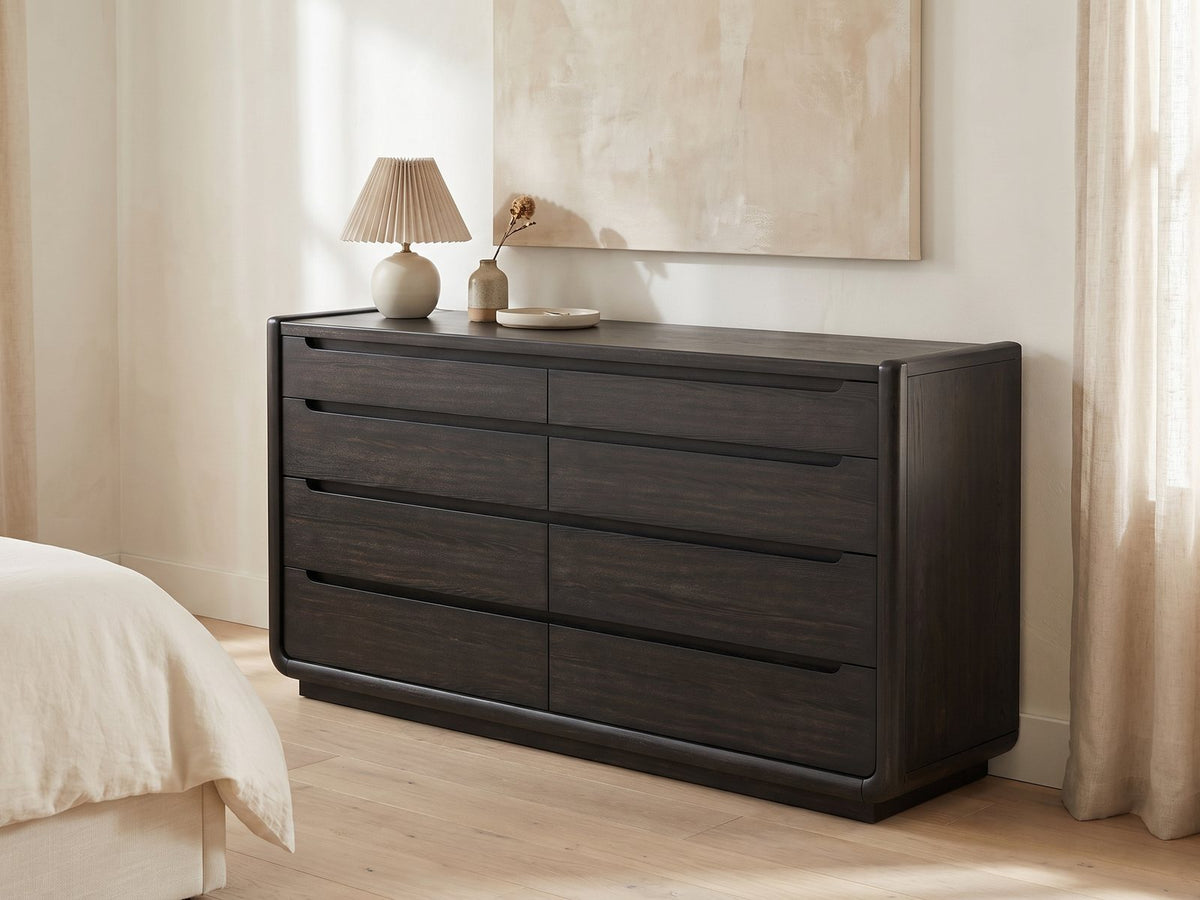 Conegliano 66-Inch Burnished Black 8-Drawer Dresser against a plaster wall under an abstract canvas in a bright bedroom