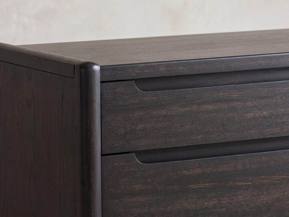 Close-up of the Conegliano 66-Inch Burnished Black 8-Drawer Dresser: the carved finger channel and the rounded corner post in burnished black ash