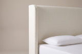 One side of the Conversano headboard: the cream boucle wing with a rounded top corner beside the plain flat panel, above a white pillow
