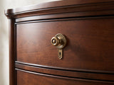 Close-up of the Cormons 66-Inch Dark Cherry and Burl 9-Drawer Dresser: the antique-brass knob on a beaded rosette above a drop keyhole escutcheon