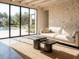 Cortona Cast Aluminum Pedestal Coffee Tables, Set of 2 seen from the side, on a jute rug in front of a linen sofa in a poolside villa