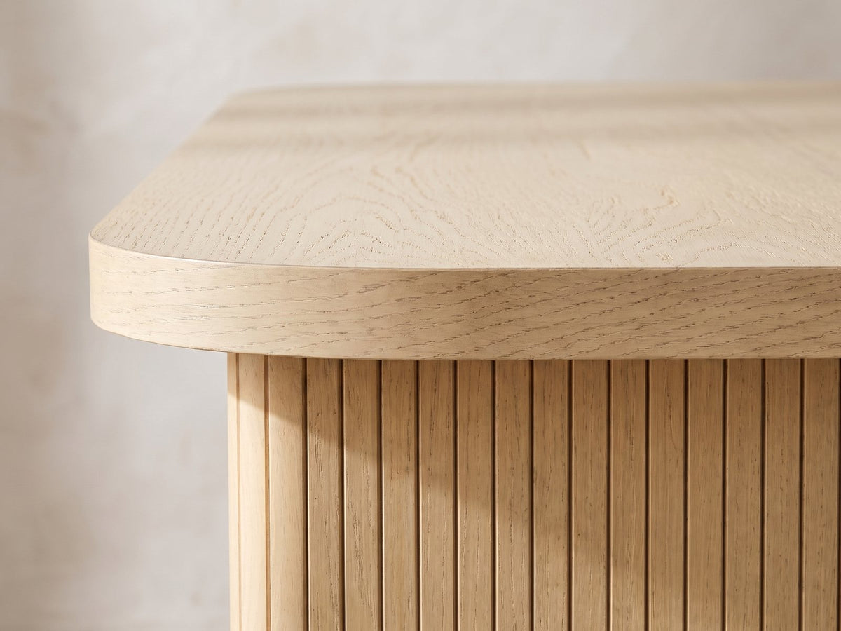 Close-up of the Cropani 69-Inch Rectangular Fluted Dining Set with 4 Arm Chairs: the rounded corner of the oak-veneer top above a fluted panel leg