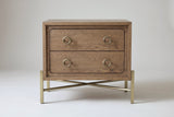 The Cuglieri nightstand in latte elm, front view on a light studio backdrop: two drawers with four brass ring pulls above a brass-tone stand with crossing rods