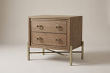 The Cuglieri two-drawer nightstand in latte elm with antique-brass ring pulls and a brass-tone metal X-base, three-quarter view on a light studio backdrop