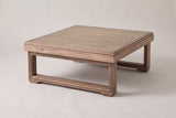 The Custonaci square acacia outdoor coffee table in a weathered brown finish, three-quarter view on a light studio backdrop