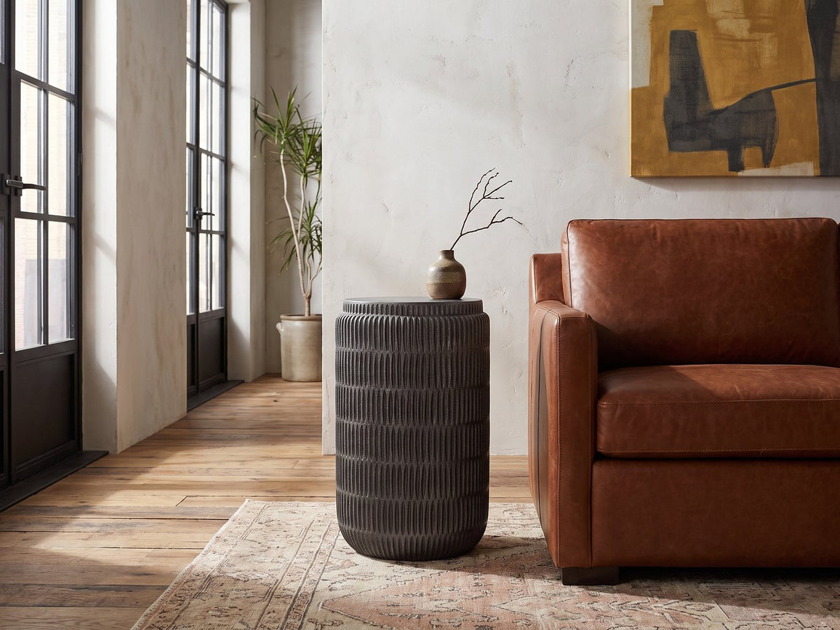 Cutigliano Cast Aluminum Carved Cylinder Side Table beside a leather sofa in an industrial loft