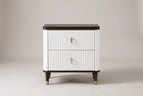The Desulo nightstand, front view on a light studio backdrop: two fluted white drawers, rounded corners, a walnut-tone top and tapered brass-capped legs