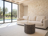 Dolceacqua Natural Braided Jute Round Pouf on a cream wool rug in front of a linen sofa in a poolside villa
