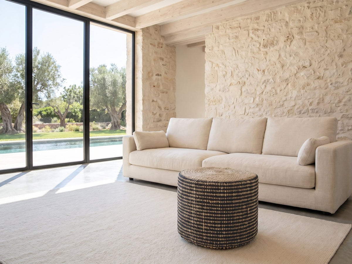 Dolceacqua Natural Braided Jute Round Pouf on a cream wool rug in front of a linen sofa in a poolside villa