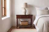 Dorgali Morocco Brown nightstand with a ceramic lamp and a seagrass basket against a white-washed adobe wall in a Santa Fe bedroom with a terracotta tile floor