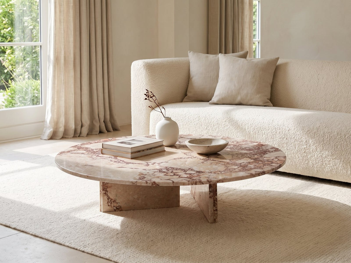 Elba Rosa Marble Coffee Table styled with books, a vase and a stone bowl in front of a cream sofa in a bright plaster room