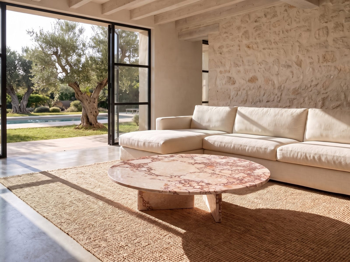 Elba Rosa Marble Coffee Table seen from the side, on a jute rug in front of a linen sofa in a poolside villa