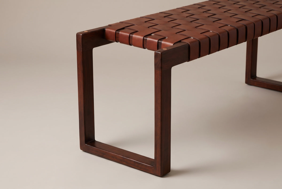 One end of the Fasano bench: the rectangular wood end frame with a small dowel plug in the top rail, and the cognac leather straps wrapping over the front edge beside it