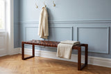 Fasano woven leather bench with a folded linen throw in a Philadelphia brownstone entry hall with a pale blue paneled wall, brass coat hooks and a herringbone oak floor