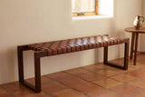 Fasano woven leather bench under a deep-set window in a Santa Fe living room with a warm white plaster wall, a terracotta tile floor and a round wooden side table