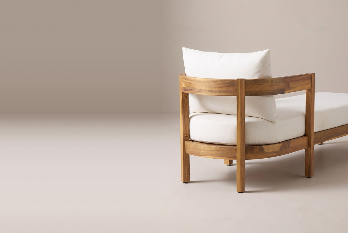 The head end of the Favignana chaise from behind: two curved acacia bands, square posts, the back pillow above the upper band