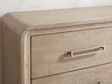 Close-up of the Feltre 62-Inch Natural Cerused Oak 6-Drawer Dresser: the open-loop brushed nickel pull on a cerused oak drawer, beside the rounded frame