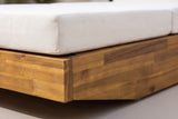 Close-up of the solid acacia base of the Ferla chaise in a teak finish, with the cream cushion resting on top