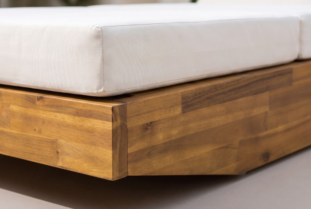 Close-up of the solid acacia base of the Ferla chaise in a teak finish, with the cream cushion resting on top