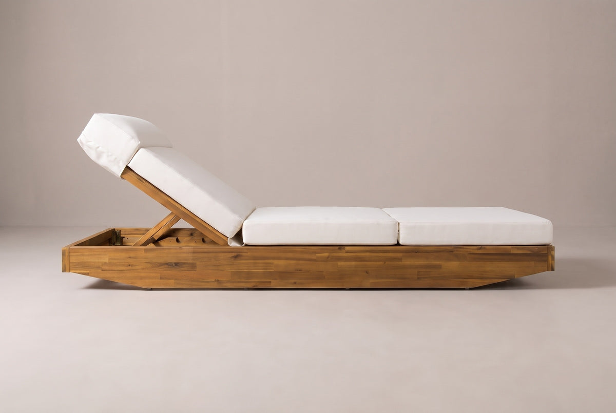 The Ferla chaise lounge seen from the side: the raised backrest and headrest on the left, the long low acacia base with angled ends