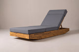 The Ferla acacia chaise lounge with a dark grey cushion, three-quarter view from the foot end on a light studio backdrop