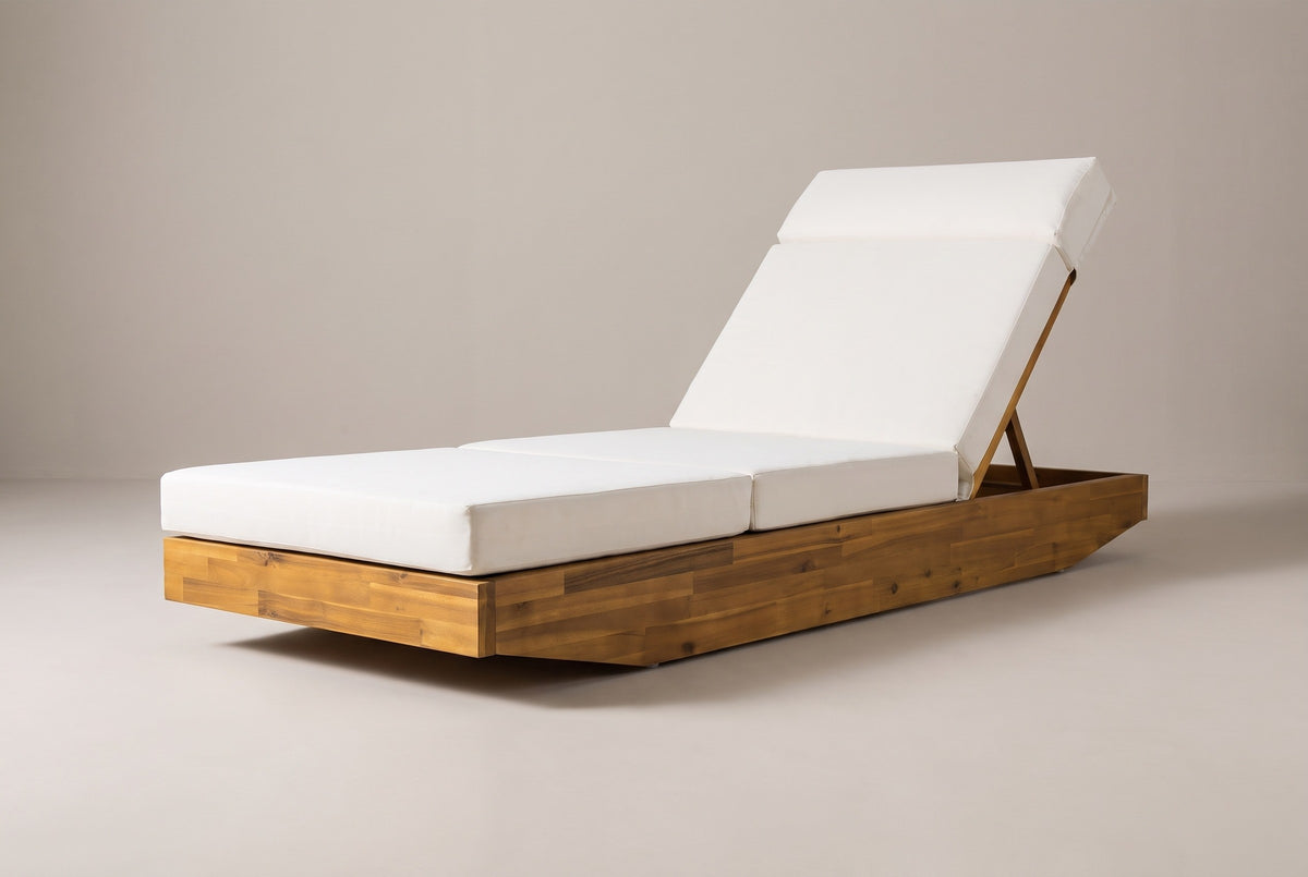 The Ferla acacia chaise lounge with a cream cushion, three-quarter view from the foot end on a light studio backdrop