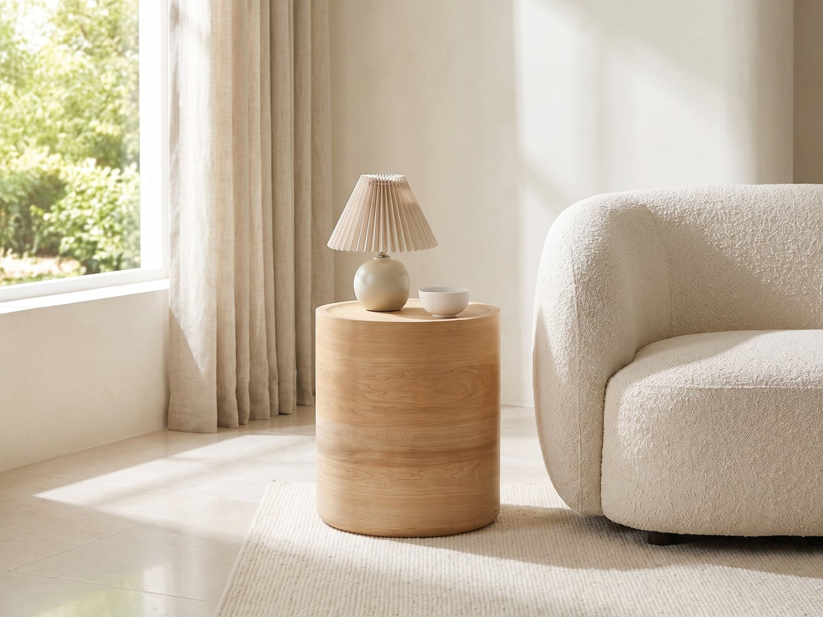 Ferrandina Natural Wood Veneer Drum Side Table with a lamp and a ceramic bowl beside a cream boucle sofa in a bright plaster room