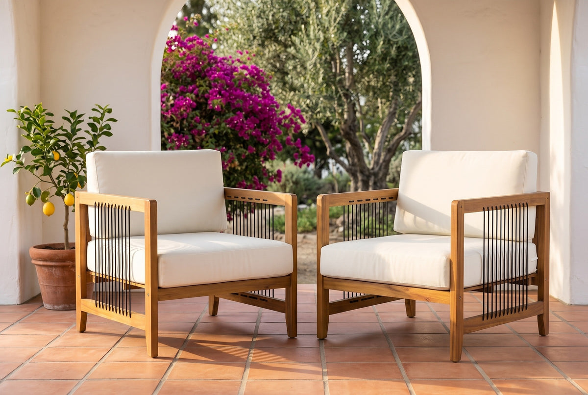 Two Ficarra acacia armchairs with ivory cushions on a terracotta tile porch, a whitewashed arch behind with bougainvillea and an olive tree beyond (planter not included)
